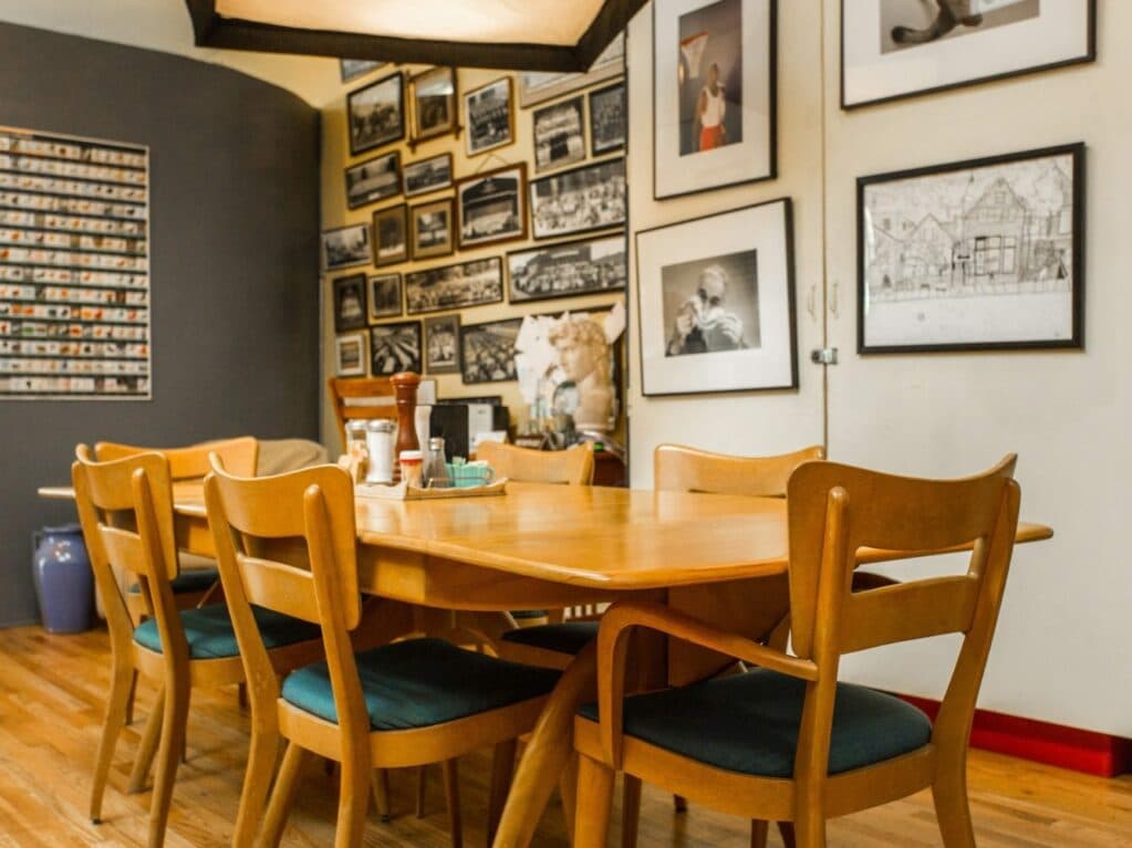A wooden dining table surrounded by chairs in a gallery-style room filled with framed photographs.