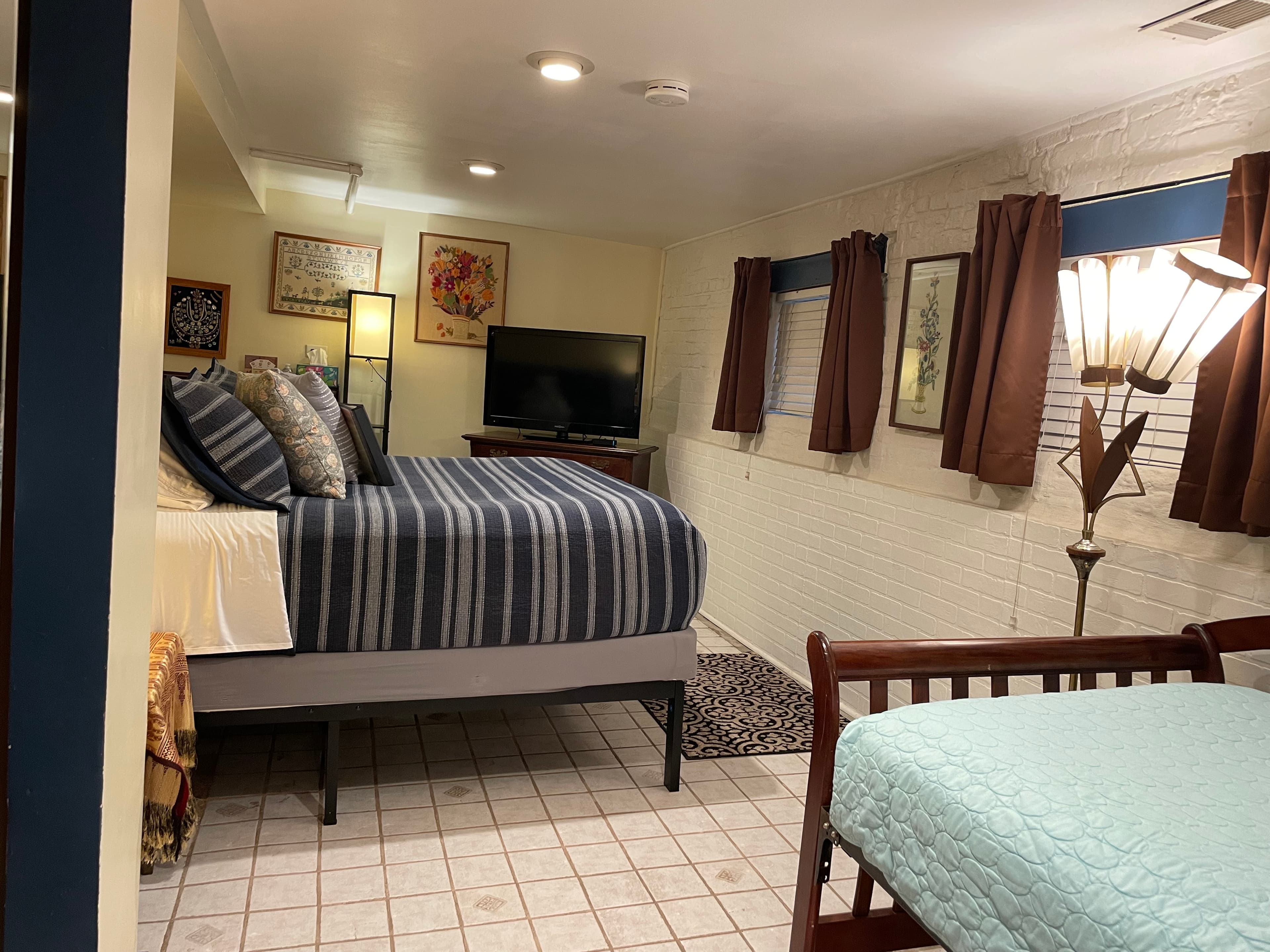 queen bed with tan sheets, brown comforter, 4 pillows, HDTV, writing desk and white robes in closet.