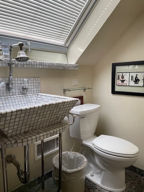 large window with black blinds, marble tiled sink and shower walls and marble tiled shelf with orange towels