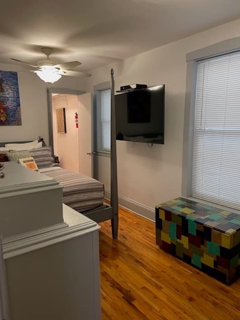 A cozy bedroom featuring a bed, a mounted TV, and a colorful storage chest.