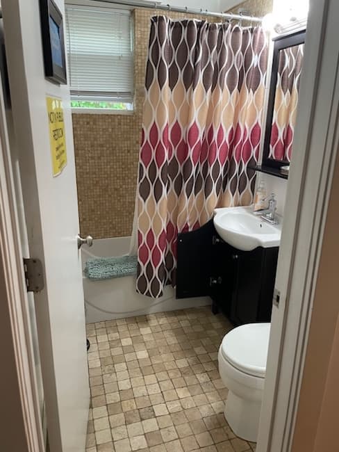 A small bathroom featuring a patterned shower curtain, a sink with a mirror, and a toilet on tiled flooring.