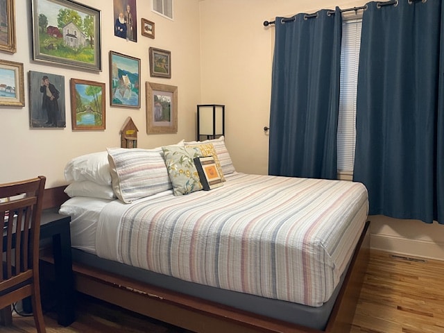 King bed with tan sheets and dark brown comforter with tan walls with old original paintings on wall. oak wood floors