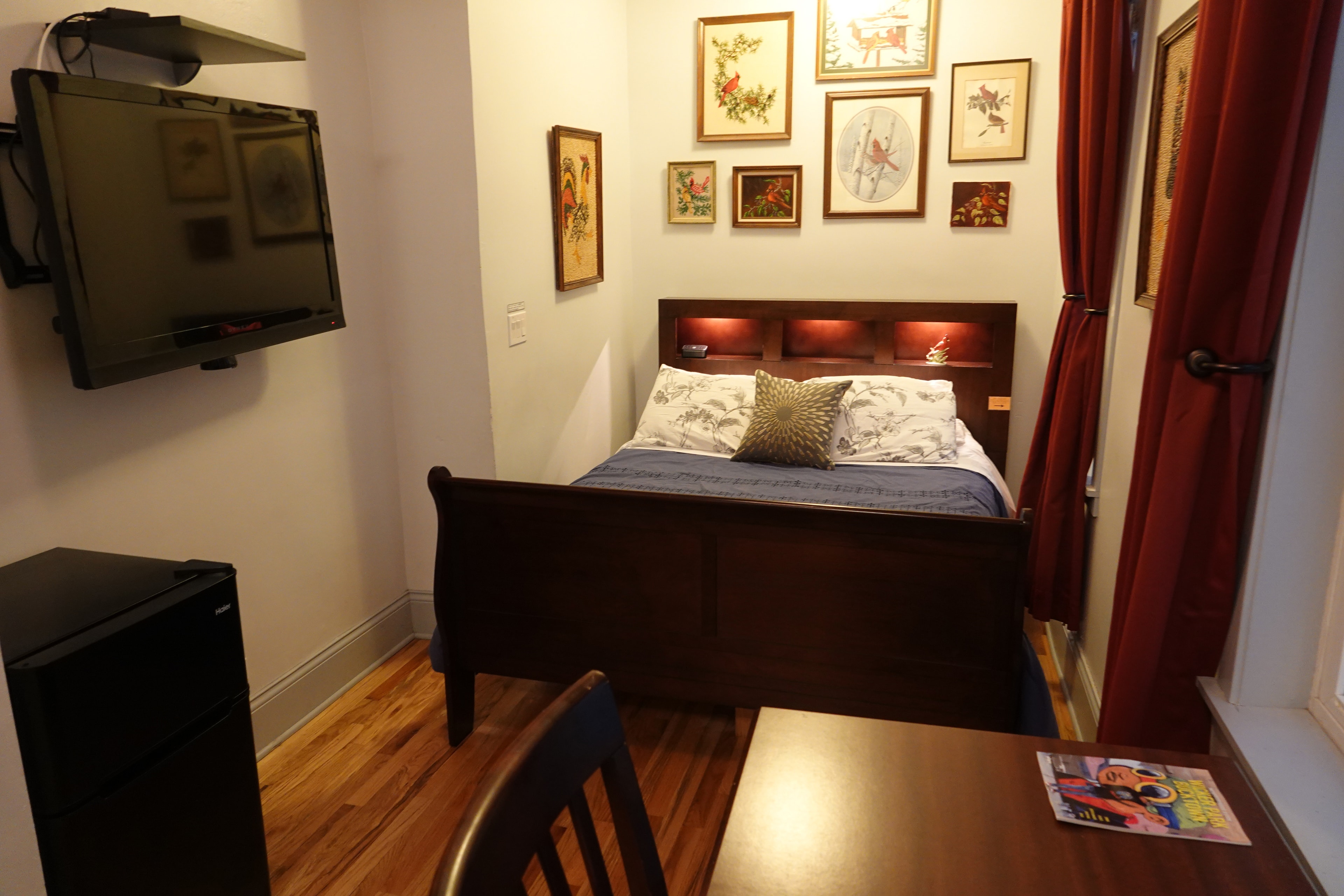 queen bed with wood bed frame, white robes hanging in closet, tan walls showing HDTV and paintings of cardinals