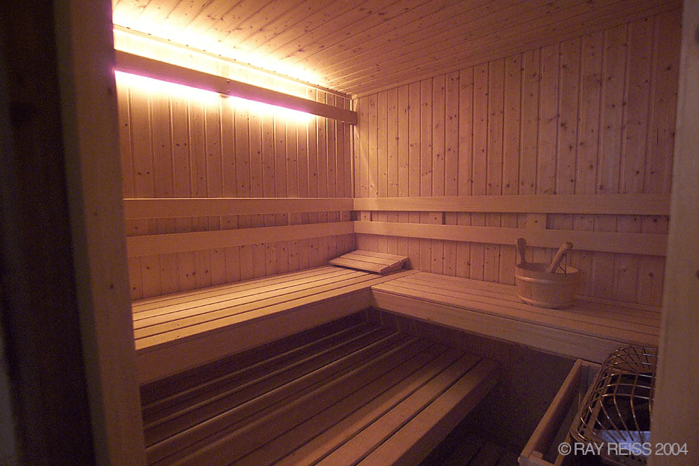 A wooden sauna interior with benches, soft lighting, and a sauna bucket.