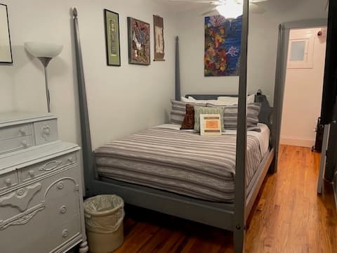 A cozy bedroom featuring a four-poster bed, striped bedding, a dresser, and decorative wall art.