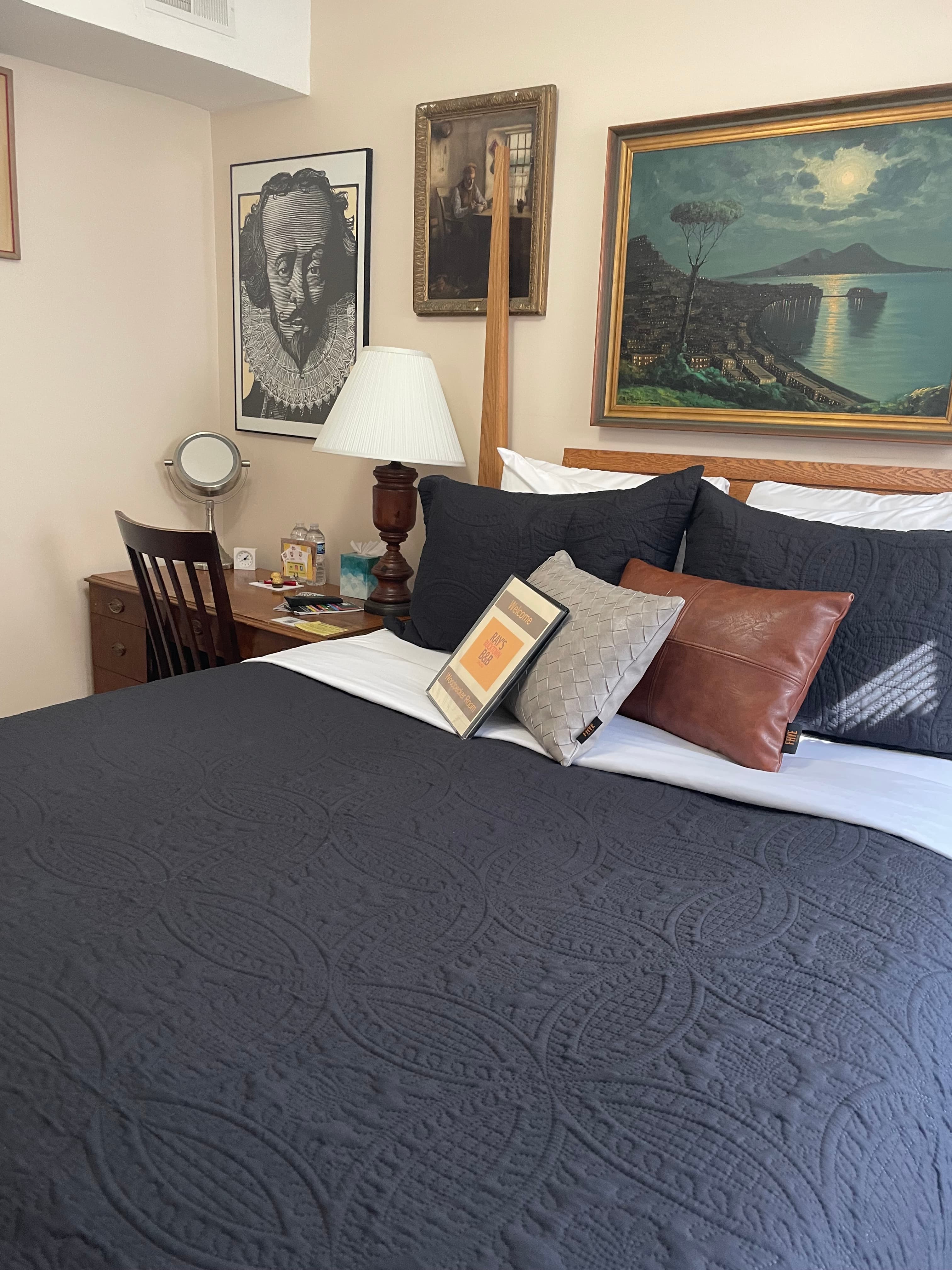 A cozy bedroom featuring a dark quilted bedspread, decorative pillows, and artwork on the walls.