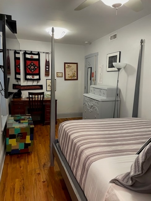 A neatly arranged bedroom featuring a four-poster bed, colorful accent furniture, and various wall art.