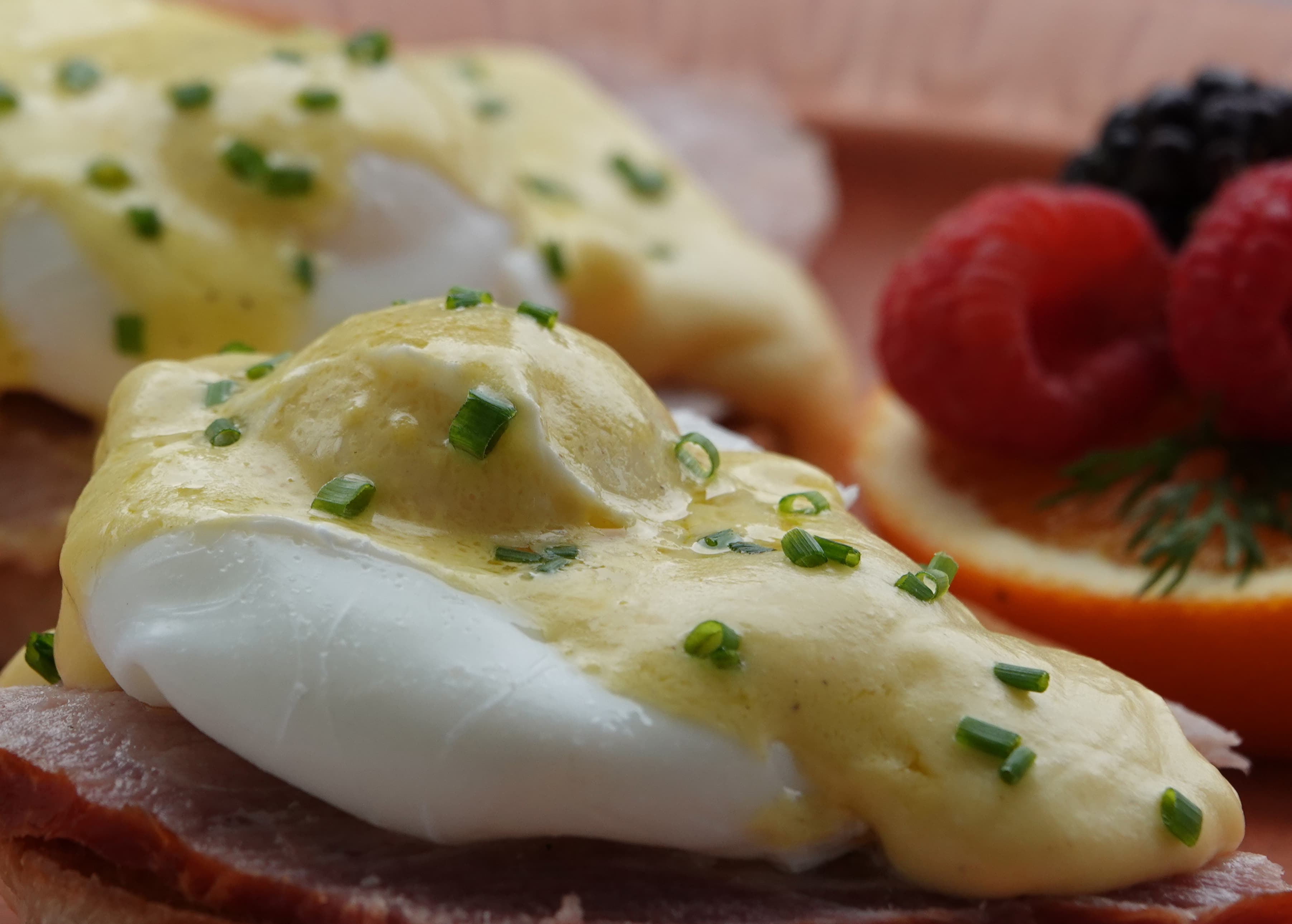 Poached eggs topped with hollandaise sauce and chives, served with fresh berries and citrus slices.