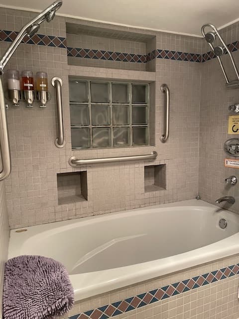 Grey deep ub with 4 shower heads, red/brown shower cumin and glass block inset with neon that says "ray's"