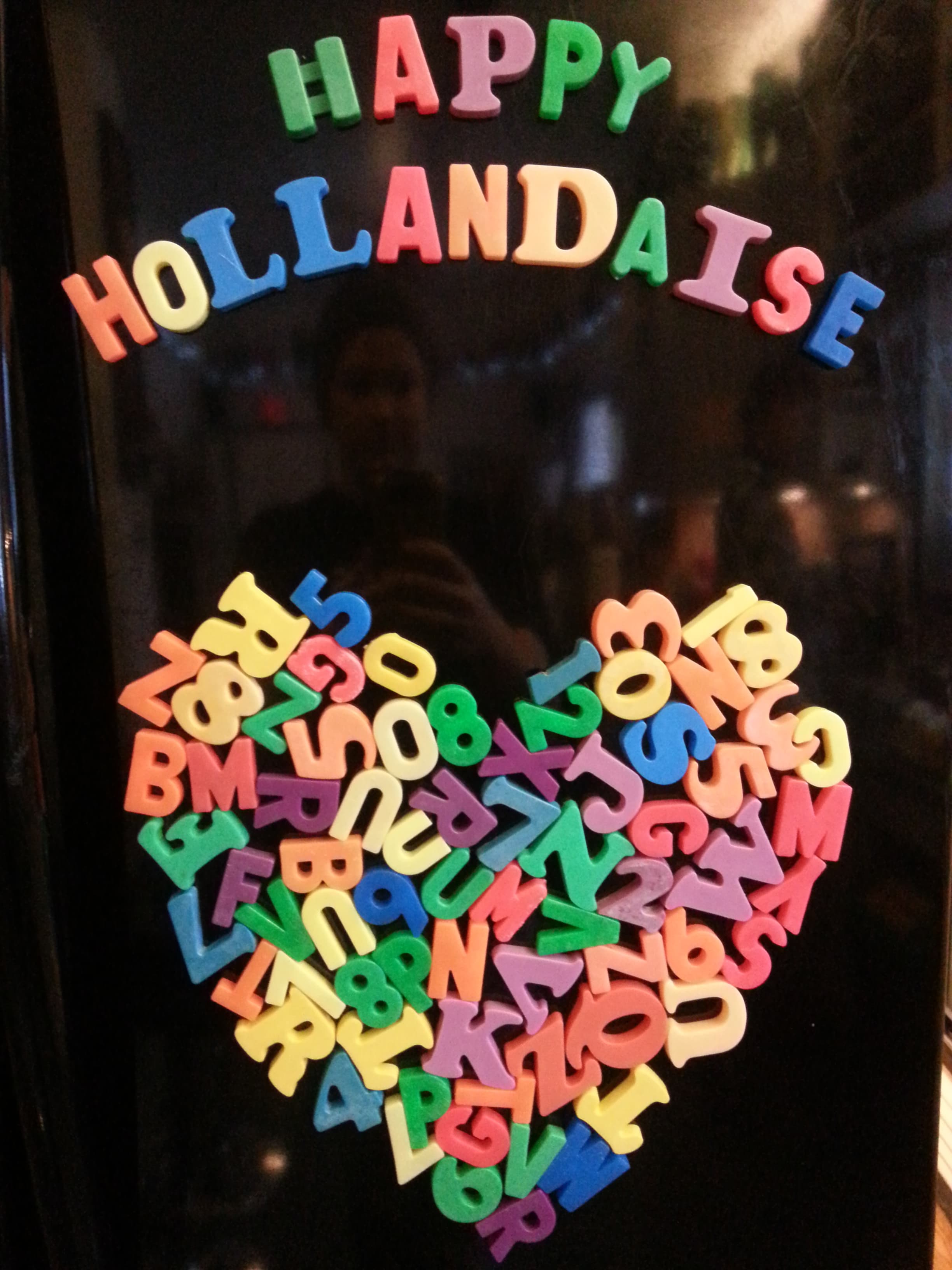 Colorful magnetic letters on a fridge spell out "HAPPY HOLLANDAISE" above a heart made of various letters and numbers. Colorful magnetic letters on a fridge spell out "HAPPY HOLLANDAISE" above a heart made of various letters and numbers.