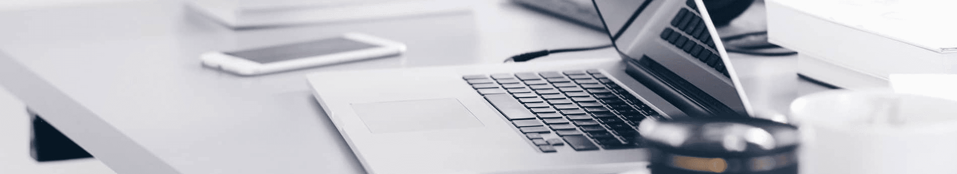 A laptop is open on a desk alongside a smartphone and a mug.