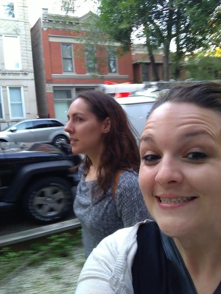 Two women walk down a street, one smiling at the camera while the other appears focused ahead. Two women walk down a street, one smiling at the camera while the other appears focused ahead.