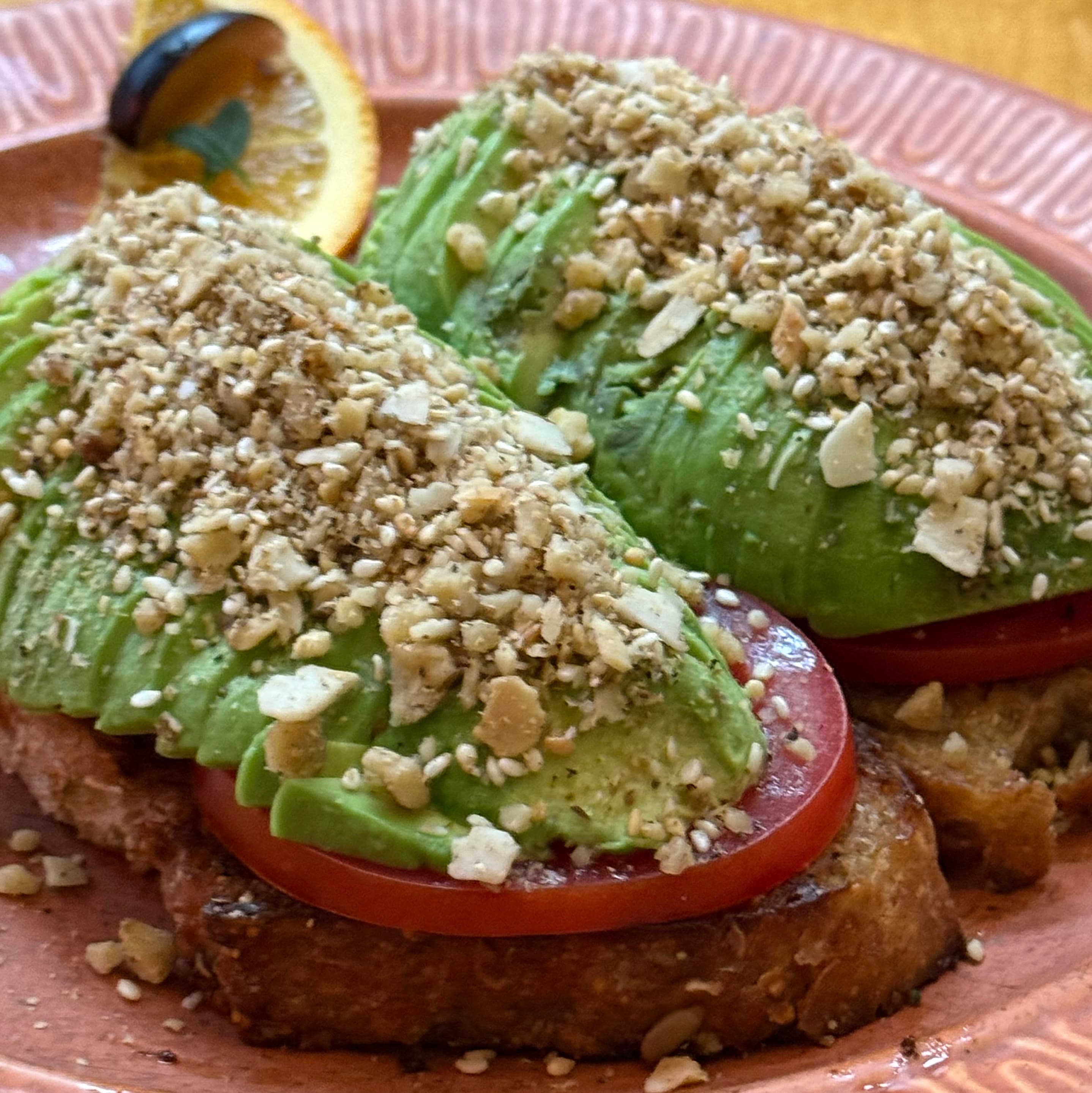 Avocado toast topped with chopped nuts and served with a slice of orange.