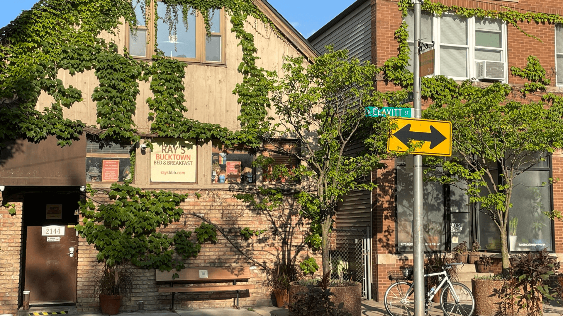 A quaint bed and breakfast covered in greenery, located at the corner of a street sign.