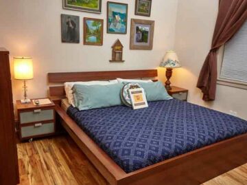 Chickadee room features hardwood floors, two nightstands, a dresser, and a king bed with blue sheets and pillows. Walls have art. There is a window to the left of the bed.